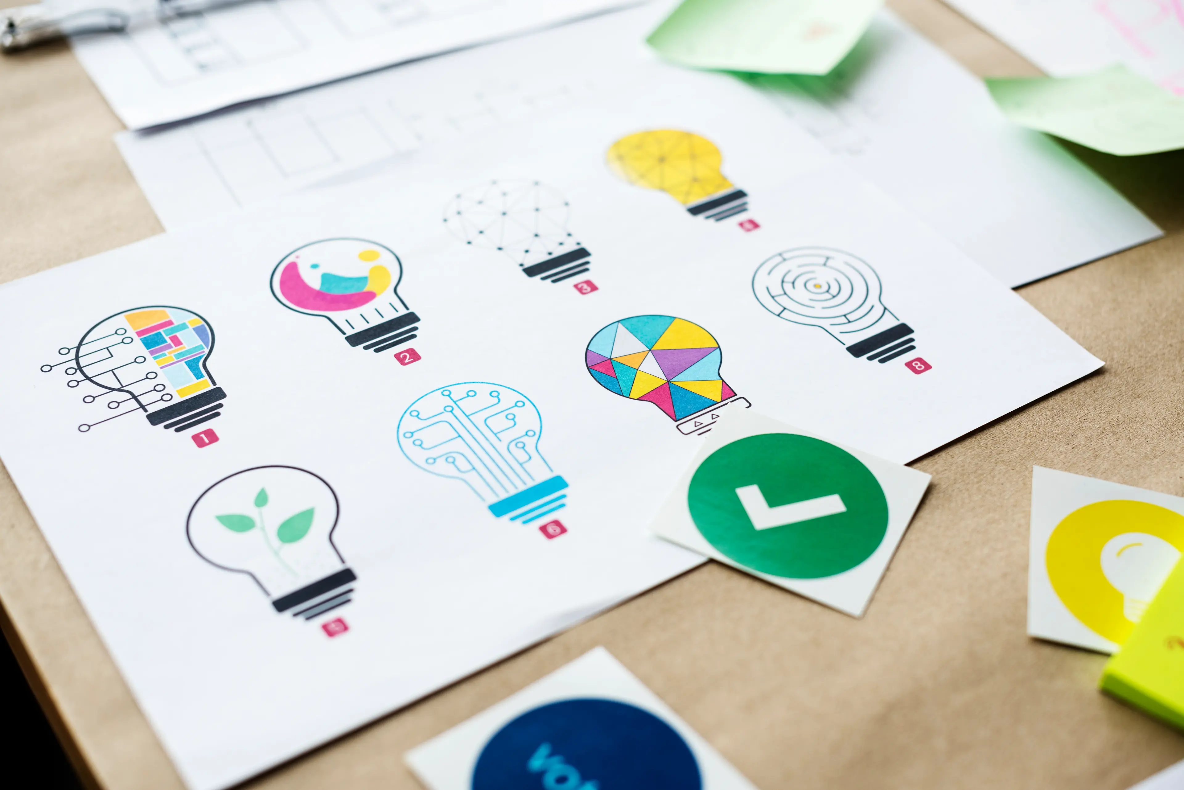 Colorful light bulb concept designs printed on paper on a design desk