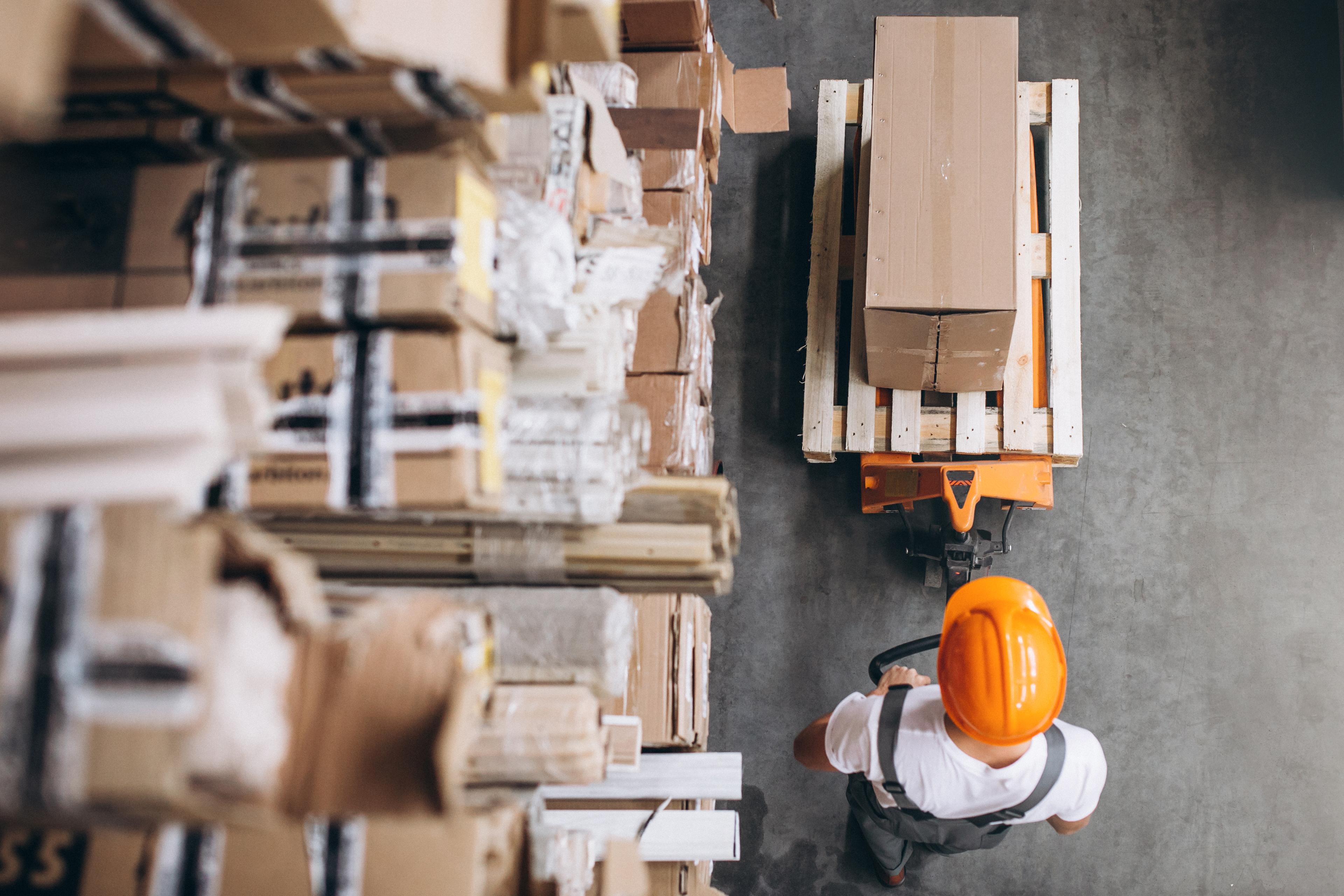 Illustrative overhead view of a warehouse worker moving cartons on a pallet jack